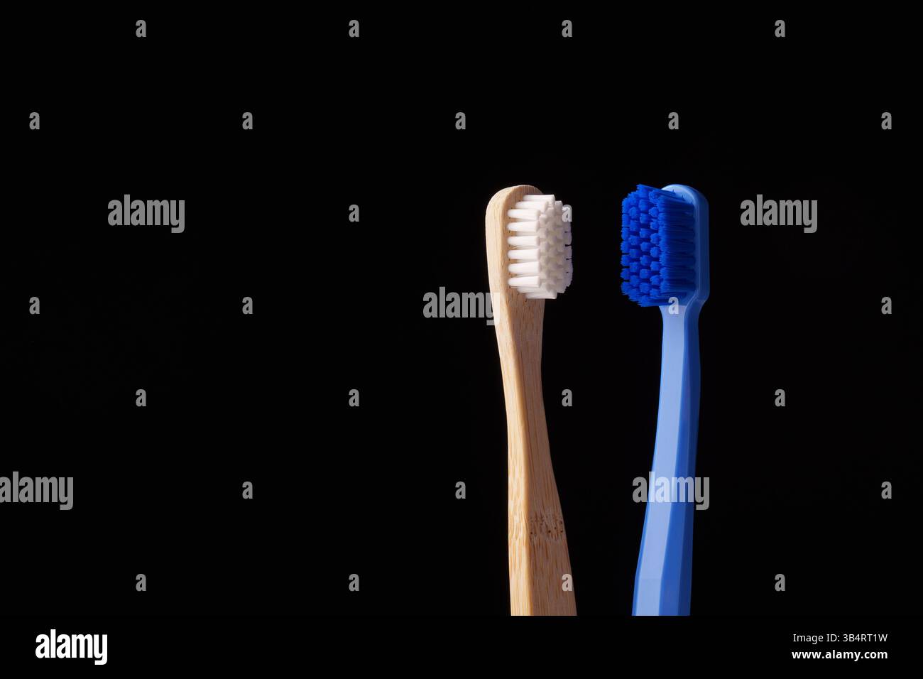Zwei Zahnbürsten, eine aus Bambus und die andere aus blauem Kunststoff, auf schwarzem Hintergrund. Umweltprobleme. Stockfoto