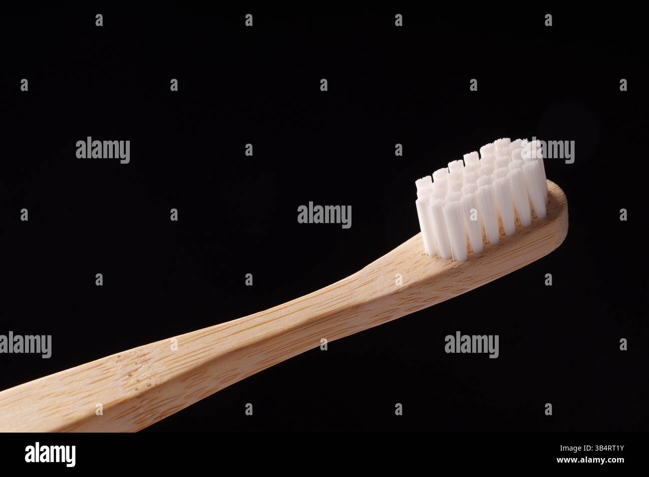 Bambus-Holzzahnbürste mit weißen Borsten auf schwarzem Hintergrund. Umweltprobleme. Minimalismus. Stockfoto
