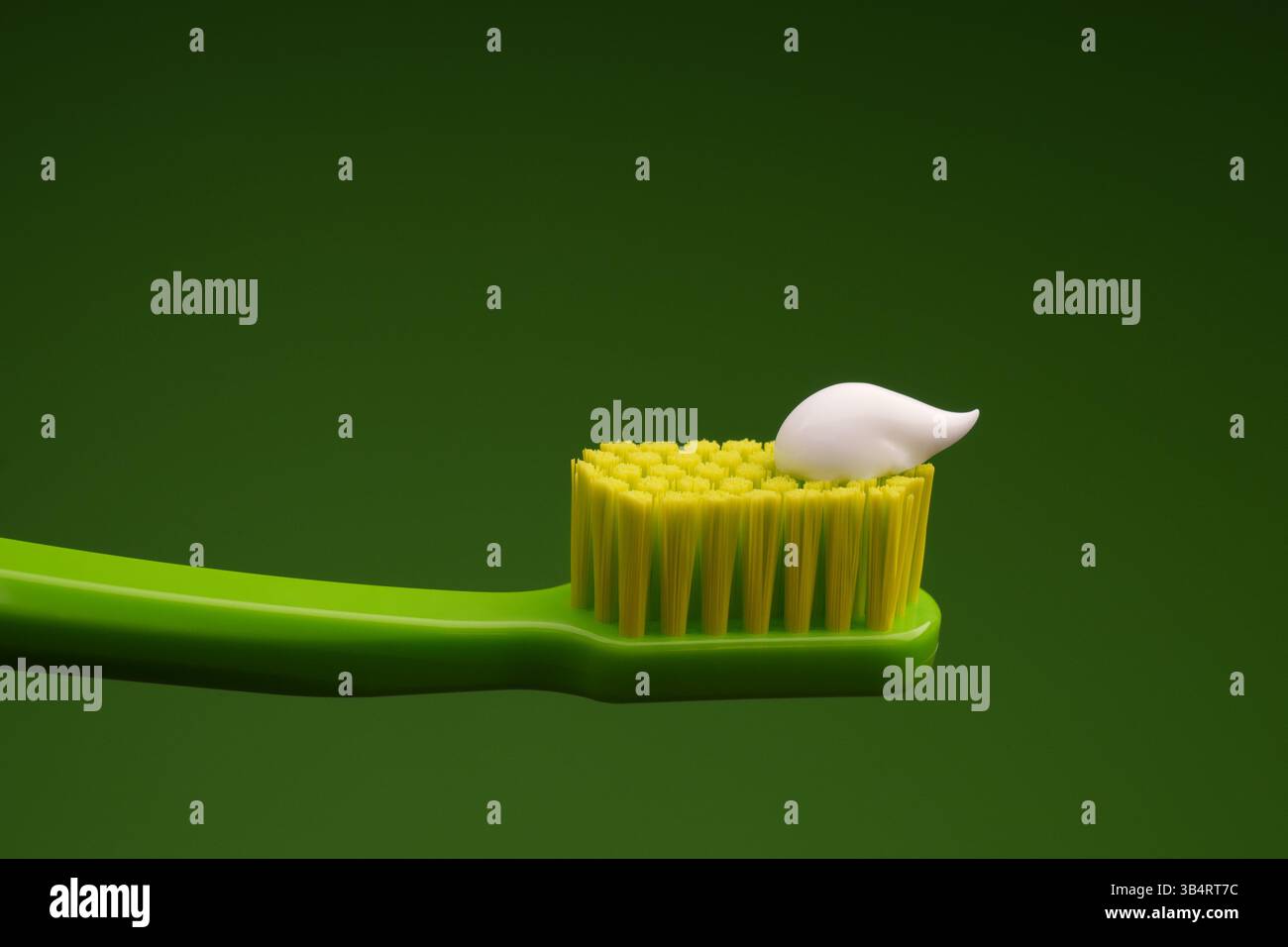Grüne Plastikzahnbürste mit weißer Zahnpasta auf grünem Hintergrund. Mundgesundheit. Stockfoto