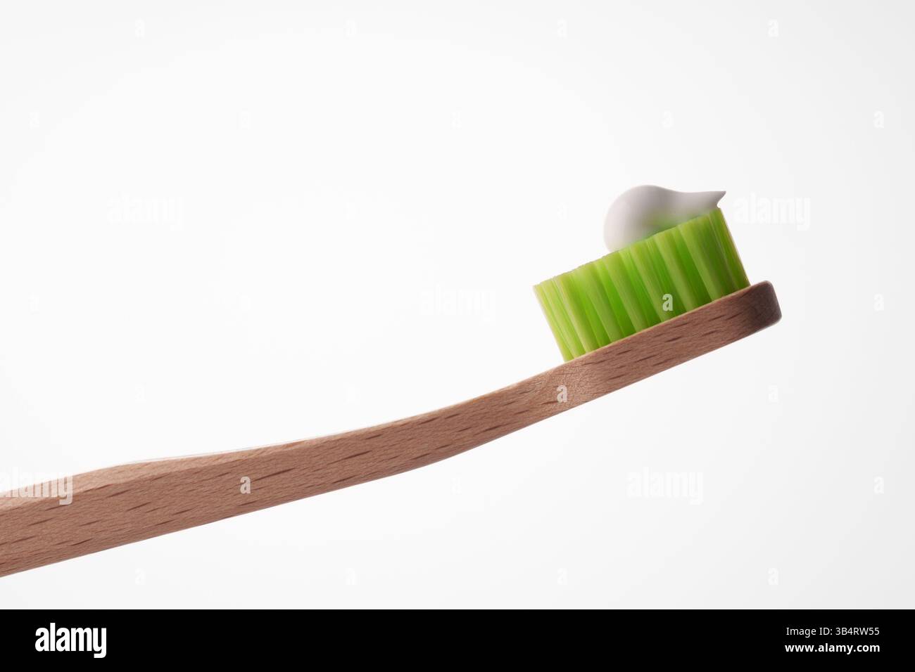 Eine hölzerne Zahnbürste mit grünen Borsten und einem Tropfen weißer Paste auf hellweißem Hintergrund. Der Zahnarzt empfiehlt es. Stockfoto