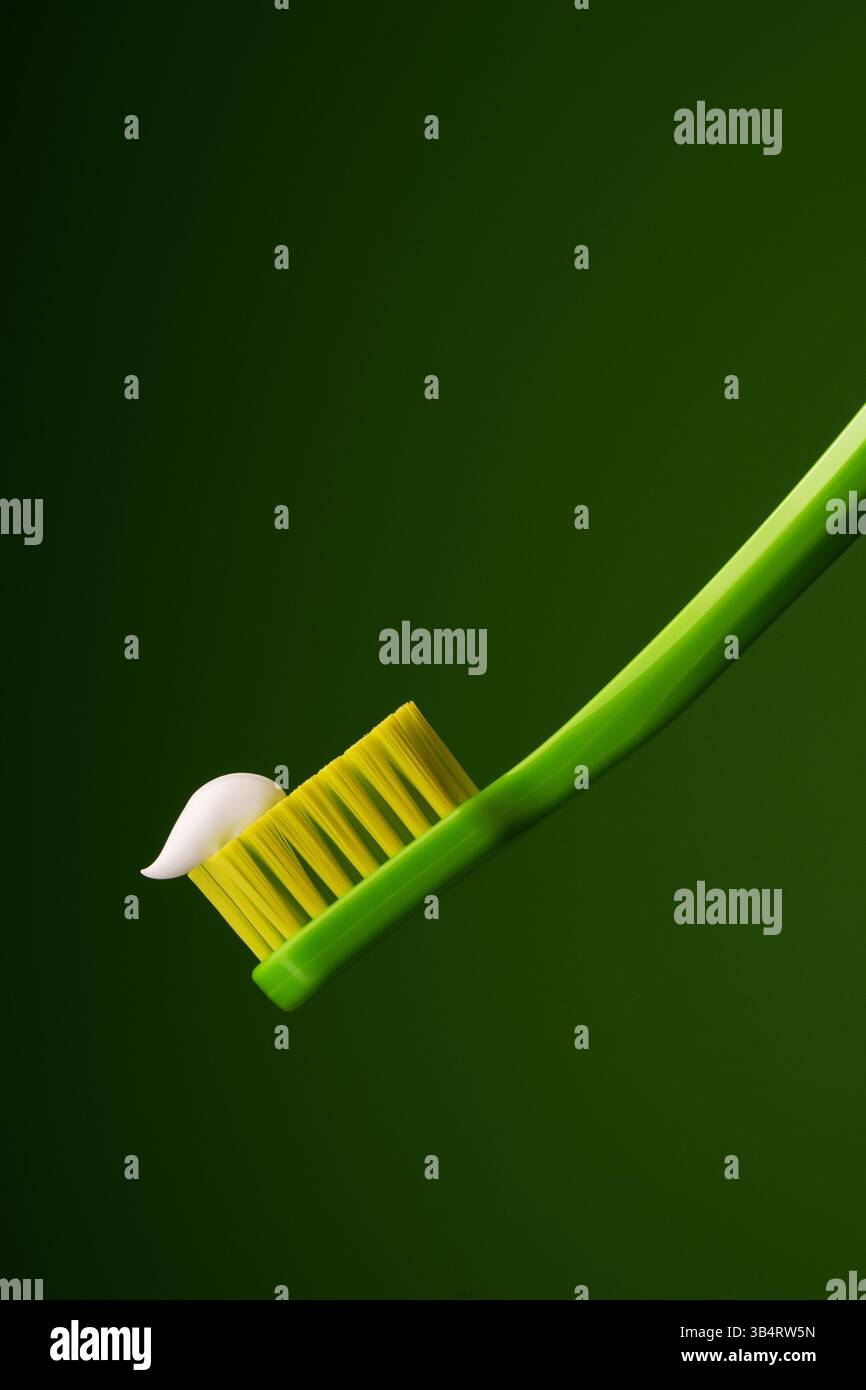 Grüne Plastikzahnbürste mit weißer Zahnpasta auf grünem Hintergrund. Mundgesundheit. Stockfoto