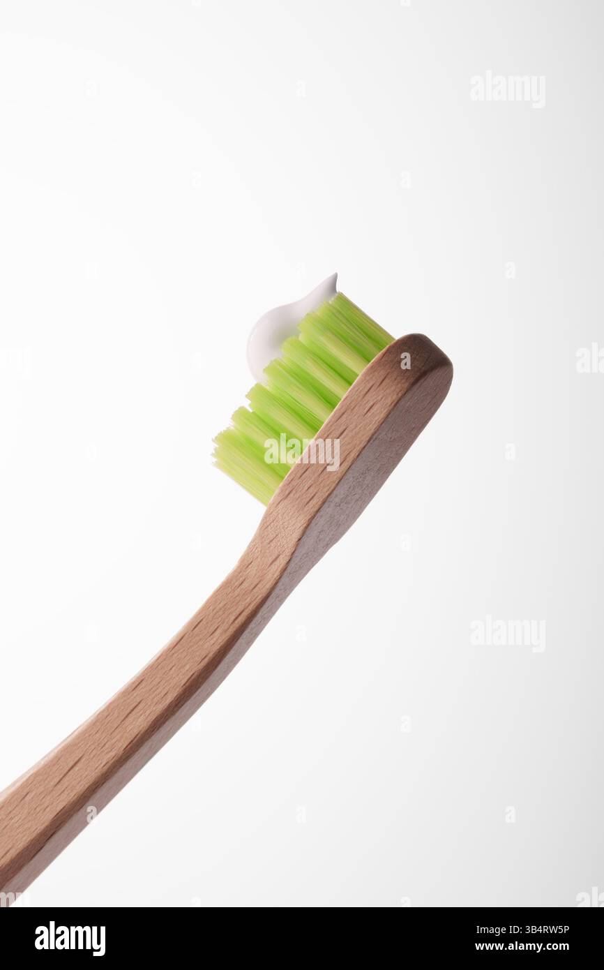 Eine hölzerne Zahnbürste mit grünen Borsten und einem Tropfen weißer Paste auf hellgrauem Hintergrund. Mundhygiene. Stockfoto