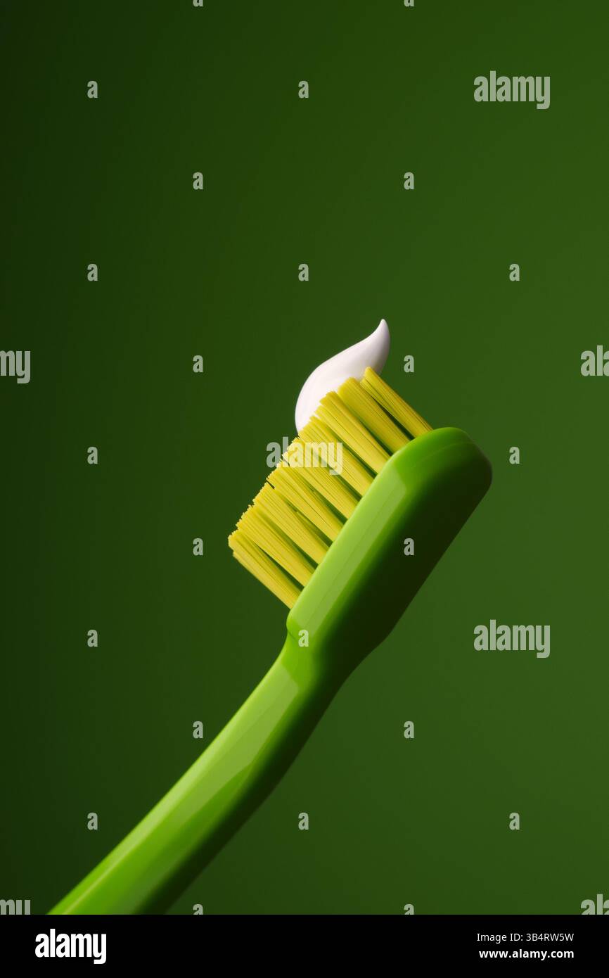Grüne Plastikzahnbürste mit weißer Zahnpasta auf grünem Hintergrund. Mundgesundheit. Stockfoto