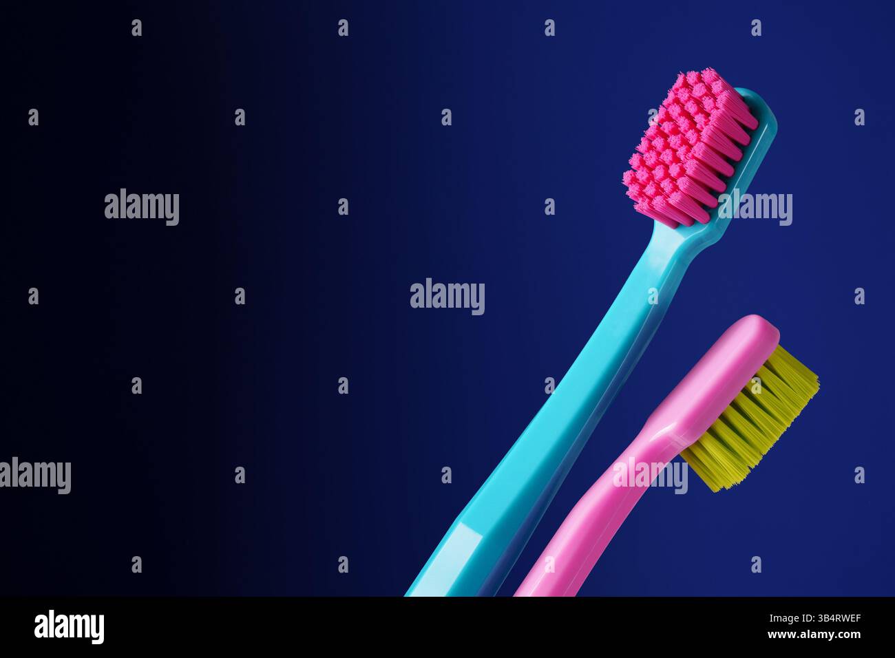 Es gibt einen Platz für Text. Zwei helle Plastikzahnbürsten auf dunkelblauem Hintergrund. Stockfoto
