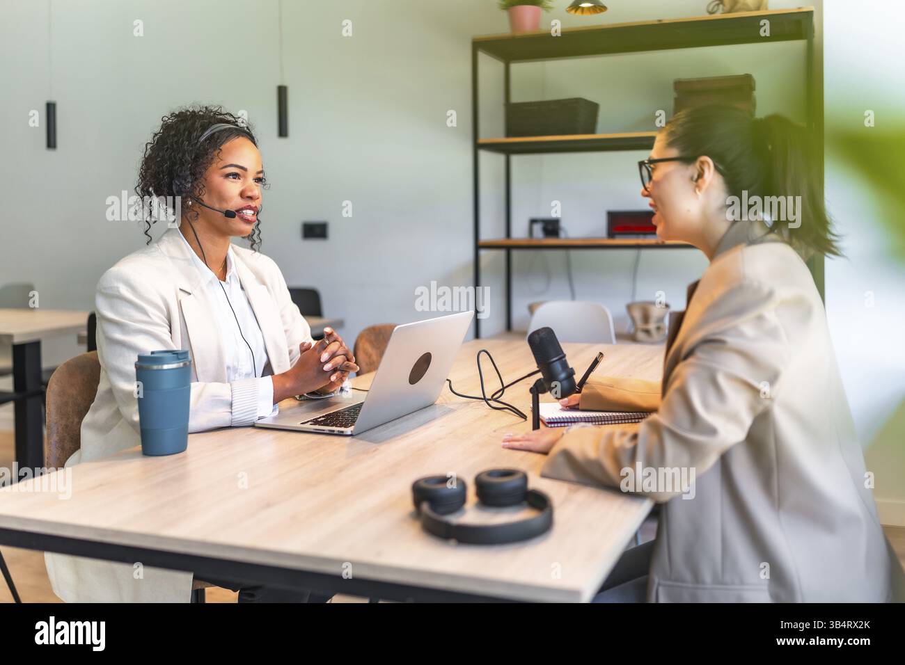 Zwei weibliche Podcasterinnen nehmen ein Interview in einem professionellen Studio mit Laptop und Mikrofon auf Stockfoto