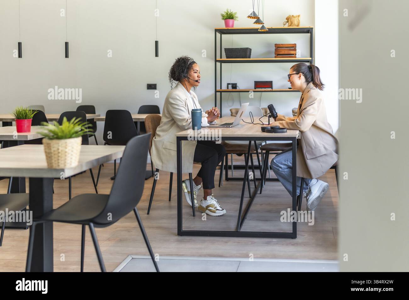 Zwei weibliche Podcaster nehmen in einem modernen Büro einen Podcast mit einem professionellen Mikrofon und Laptop auf Stockfoto