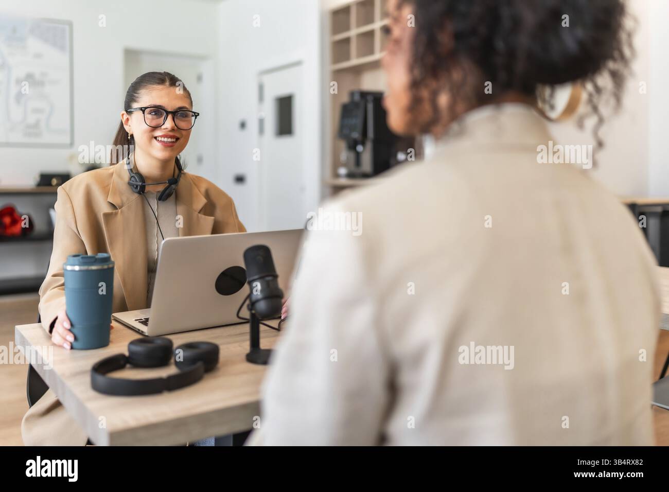Zwei Podcaster nehmen eine neue Episode in einem modernen Büro mit einem Laptop und einem professionellen Mikrofon auf Stockfoto