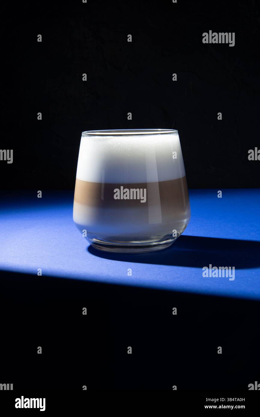Latte-Kaffee in einem transparenten Glas auf dunkelblauem Hintergrund. Studio-Beleuchtung verwendet. Stockfoto