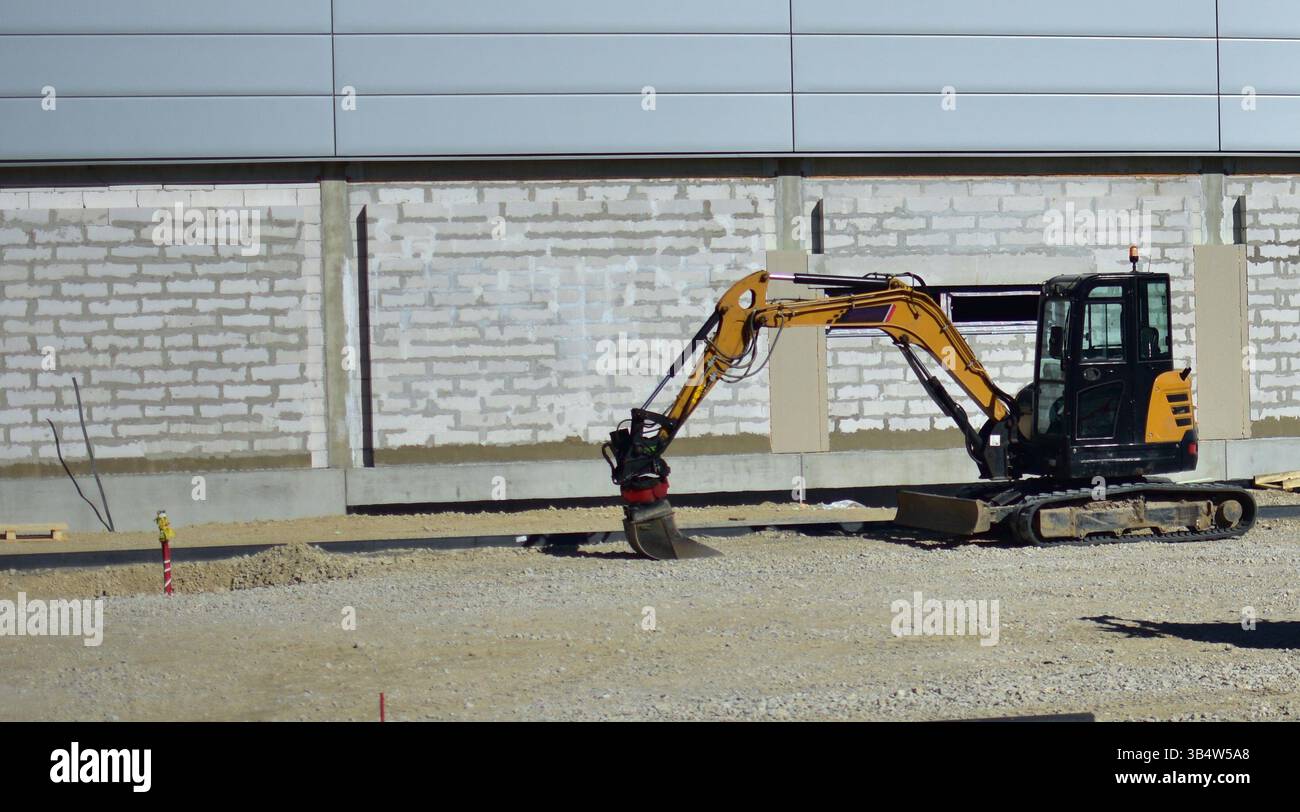 Minibagger Grabfläche auf der großen Supermarkt-Baustelle. Kleiner caterpillar-Bagger, der im Baubereich steht. Stockfoto