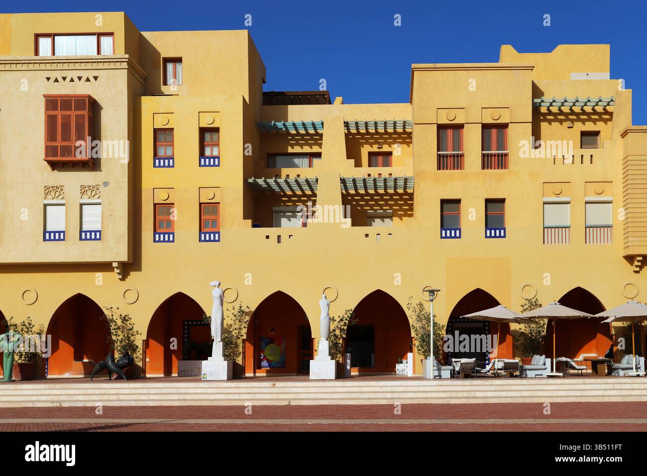 Farbenfrohe Fassade mit Bögen, Fenstern, Skulpturen und Terrassen in El Gouna, Ägypten; mediterraner-nubischer Stil unter tiefblauem Himmel. Stockfoto
