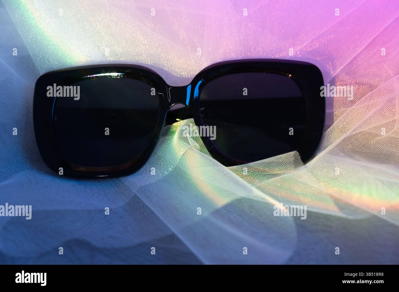 Eine elegante schwarze Sonnenbrille, die lässig auf einem eleganten weißen Tuch liegt und über eine flache Oberfläche verteilt ist, um eine gute Sichtbarkeit zu gewährleisten Stockfoto