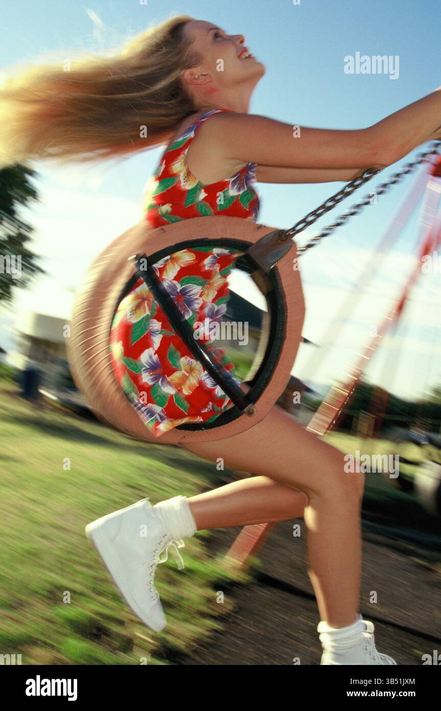 Junge Frau im Sommerkleid auf Schaukelsitz in Park Spielplatz. Stockfoto