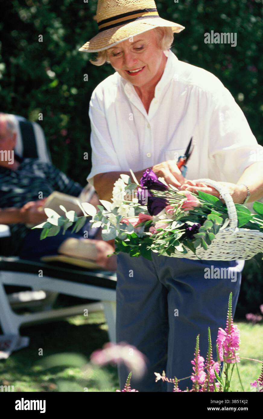 Eine ältere Frau im Garten, die einen Korb mit Schnittblumen hält. Stockfoto