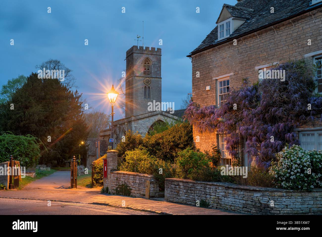 St. Marys Kirche entlang der Kirchenstraße mit einer blühenden Glyzinien auf einem Haus bei Sonnenaufgang im Frühjahr. Charlbury, Oxfordshire, England Stockfoto