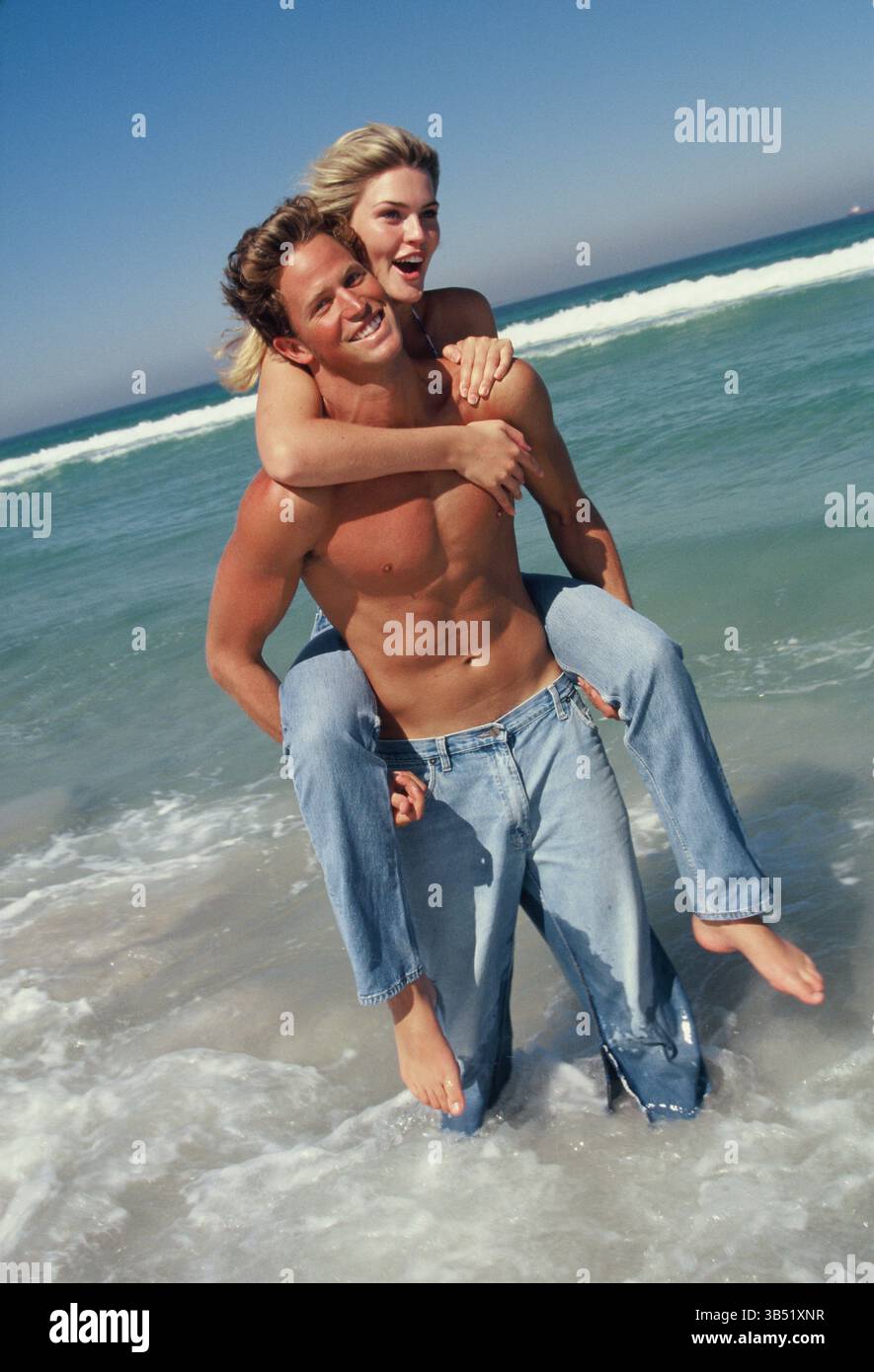 Lifestyle. Glückliches junges Paar in der Brandung. Mann, der eine Frau mit Huckepack trägt. Stockfoto