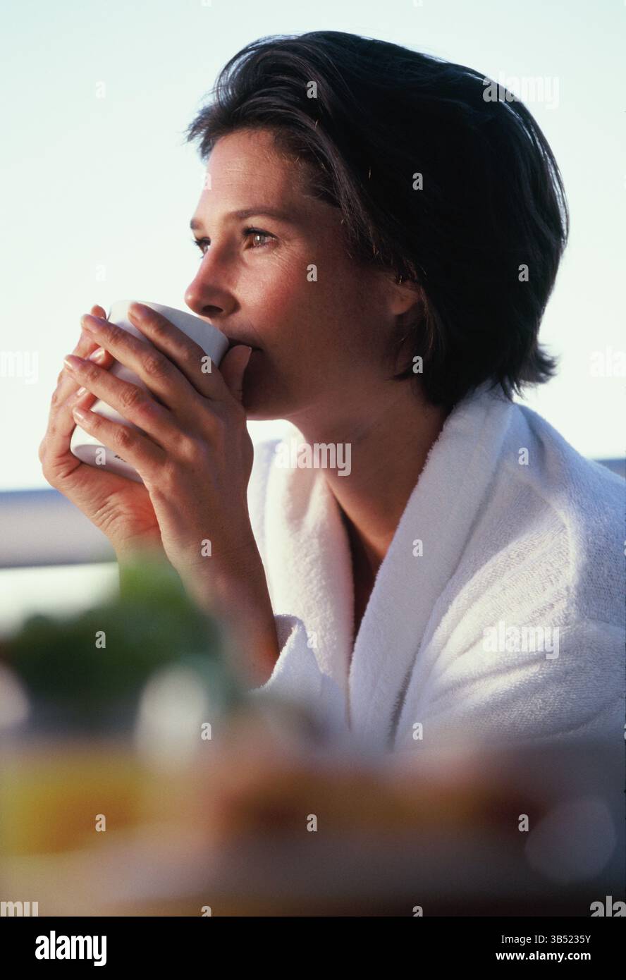 Außenprofil einer jungen Frau im Bademantel, die eine Tasse heißes Getränk hält. Stockfoto