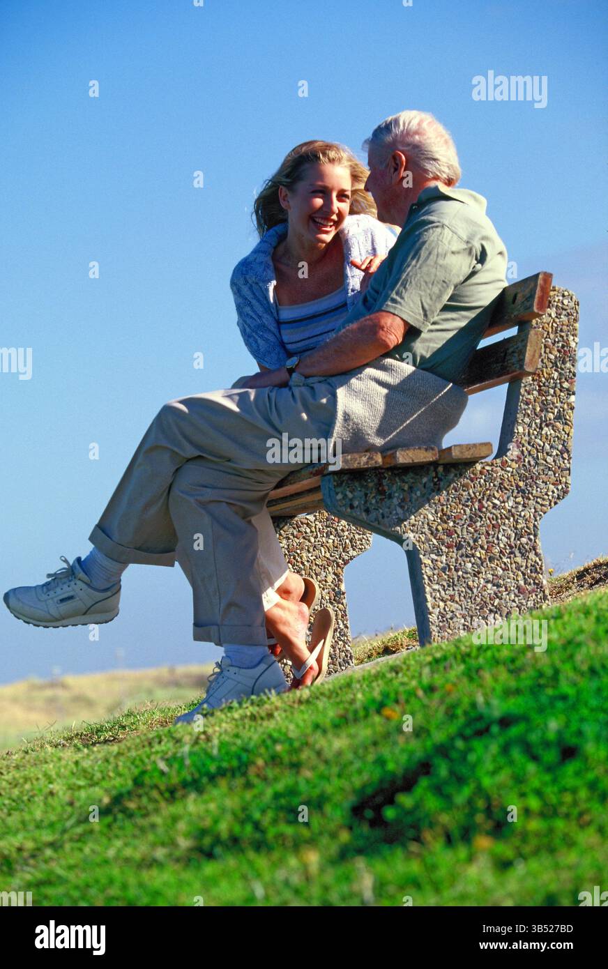 Seniorenmann mit erwachsener Tochter sitzt draußen auf einer Bank am Hügel. Stockfoto