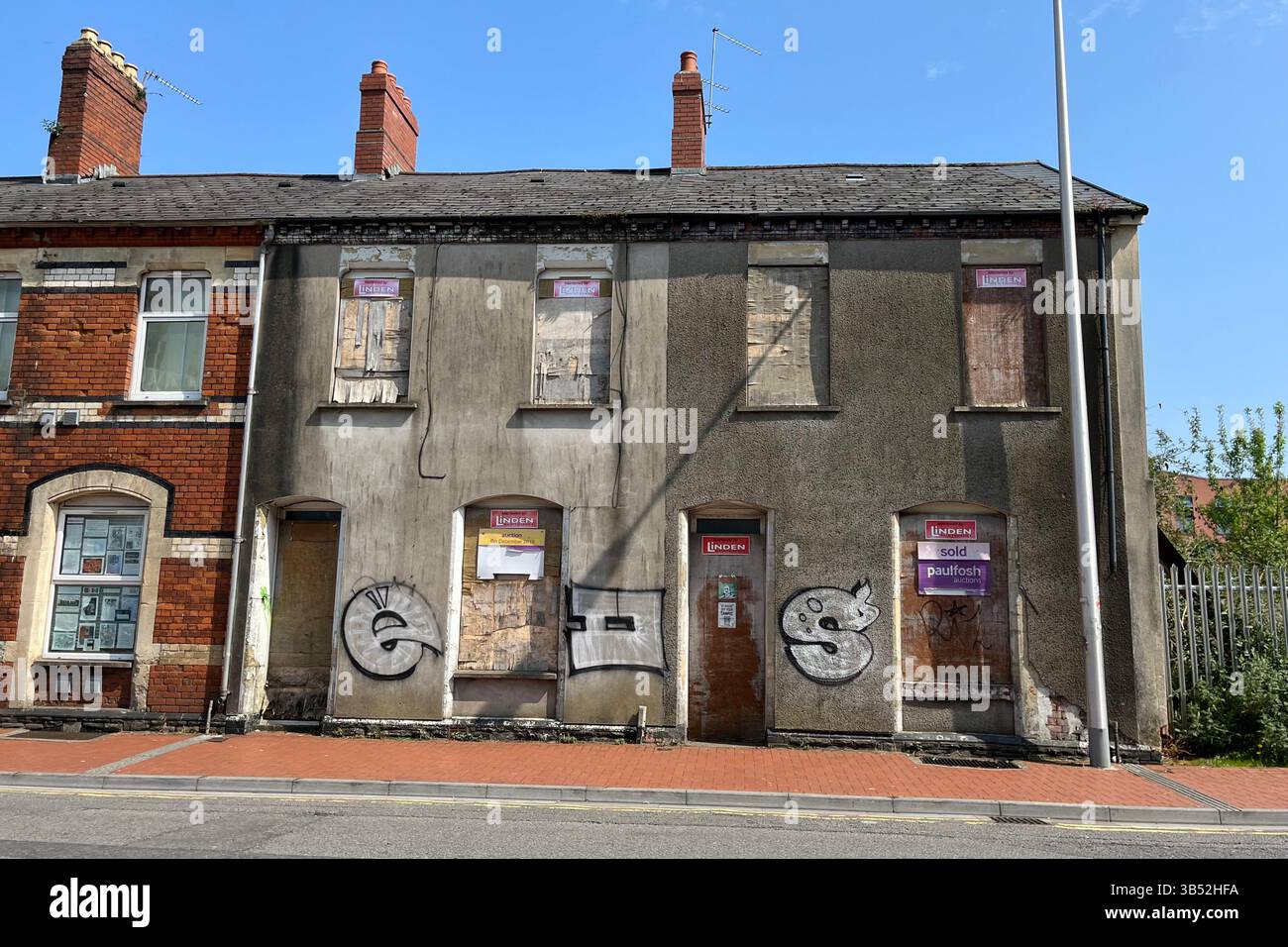 Verfallene Terrassenhäuser mit eingebauten Fenstern und Graffiti in der Nähe von Cardiff Central. Dumballs Road, Cardiff, Wales, Vereinigtes Königreich. April 2025. - Smartphone-aufgenommenes Stockfoto