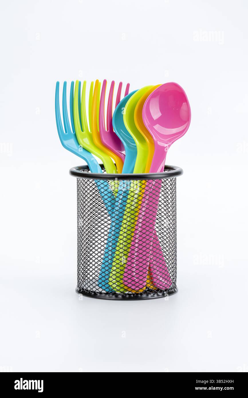 Farbenfrohes Plastikbesteck in einem eleganten schwarzen Halter, der einen lebendigen, fröhlichen Kontrast zu einem sauberen weißen Hintergrund bietet. Stockfoto