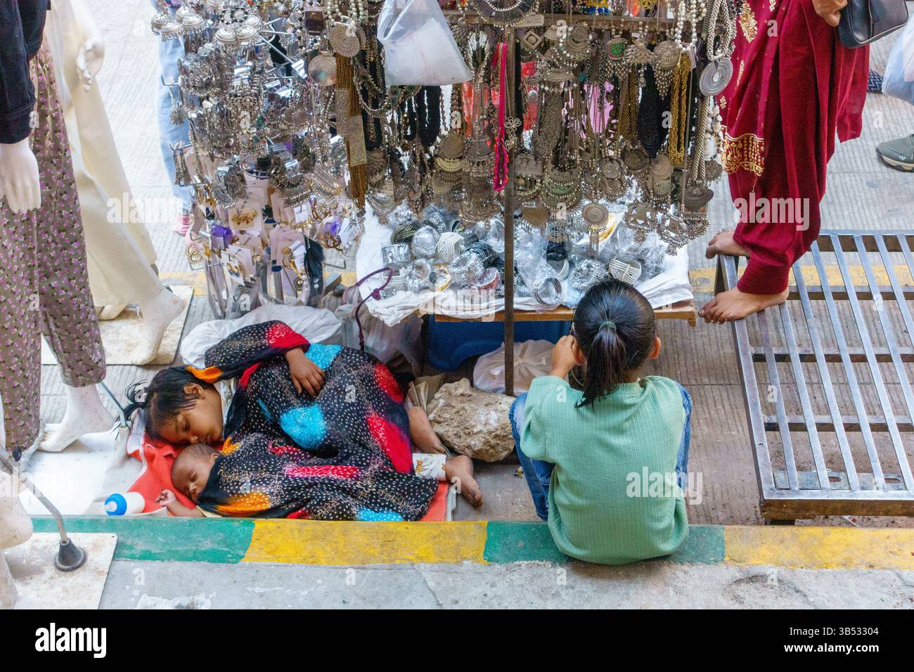 Frau, die mit ihren zwei schlafenden Babys auf dem Bürgersteig sitzt und neben ihr traditionellen Schmuck in der Church Street, Bangalore, Karnataka, Indien, Asien verkauft Stockfoto