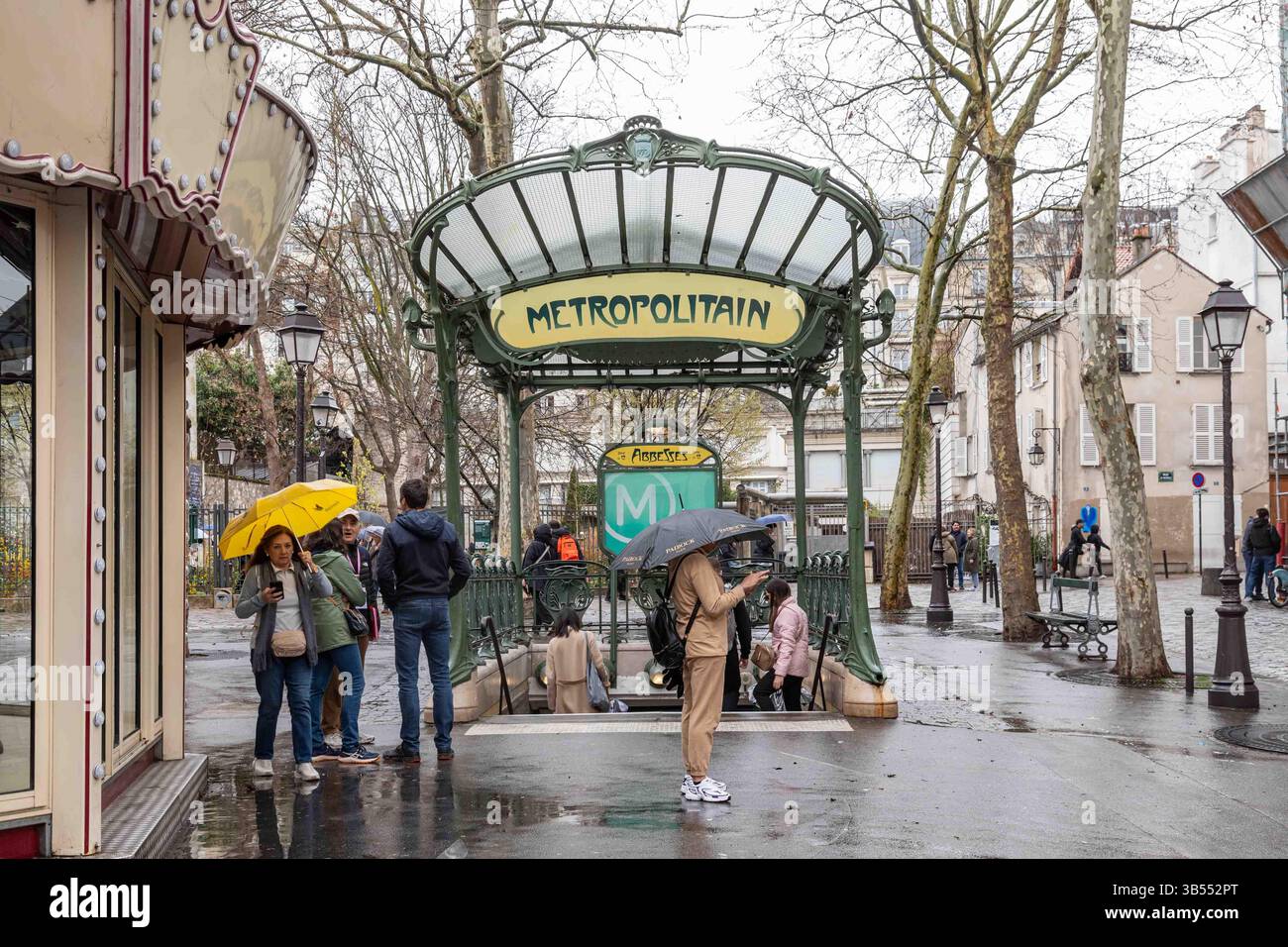 Menschen mit Sonnenschirmen vor dem Eingang der U-Bahn-Station „Abesses Art Nouveau“ an einem regnerischen Frühlingstag im Pariser Viertel Montmartre, Frankreich Stockfoto