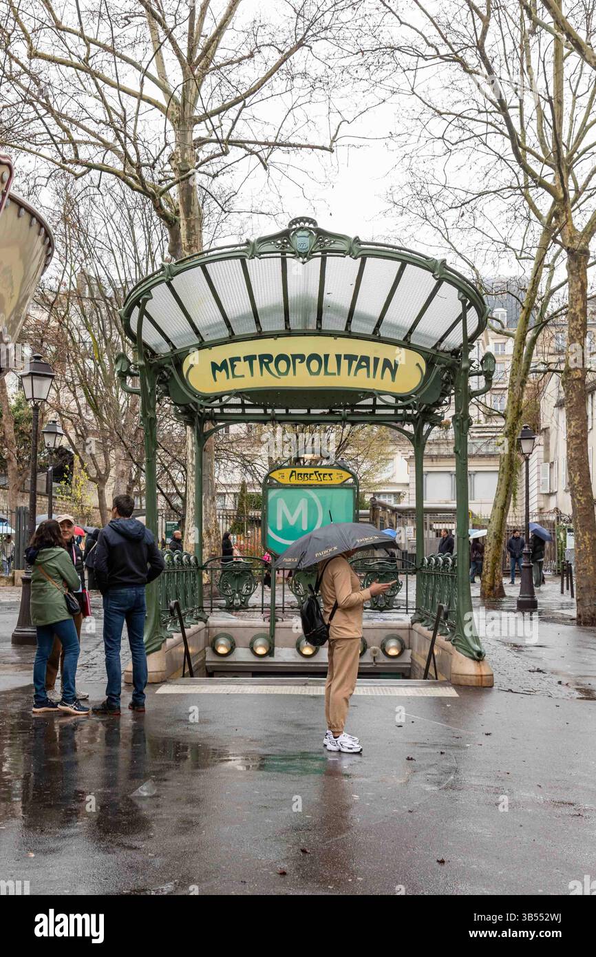 Frau mit Schirm steht vor der U-Bahn-Station Abbesses Jugendstileingang an einem regnerischen Frühlingstag im Montmartre-Viertel von Paris, Frankreich Stockfoto
