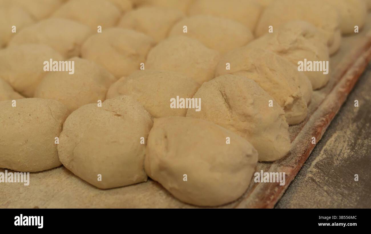 Detaillierte Ansicht der rohen Brotteigkugeln auf einem bemehlten Tablett, bereit zum Backen. Das Bild hebt die Textur des Teigs und die sorgfältige Zubereitung hervor Stockfoto