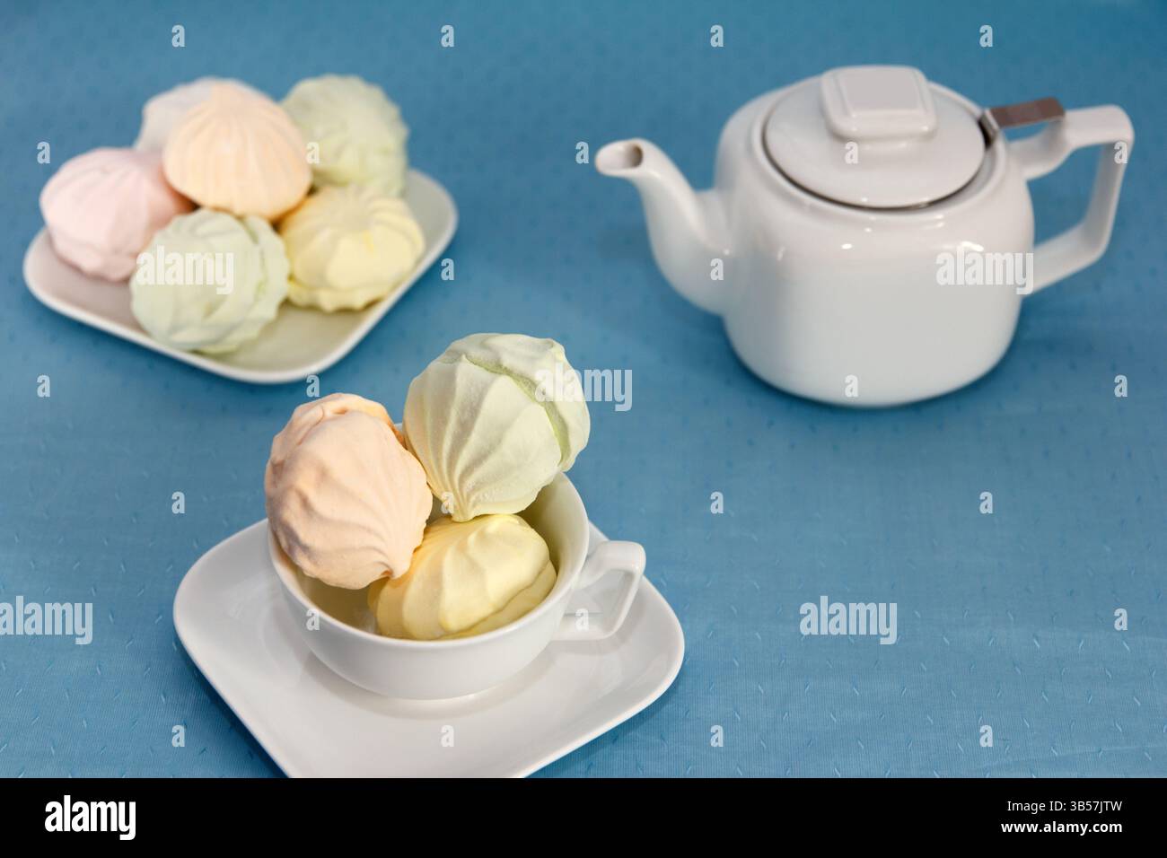 Tea Party Zeit. Auf einem gewarteten Tisch mit blauer Tischdecke liegt eine atemberaubende frische Marschlöhe und eine Teekane mit duftendem Tee Stockfoto