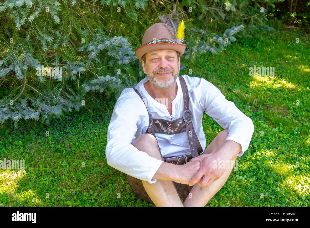 Ein älterer Mann in traditioneller tracht posiert auf einer sonnigen Lichtung Stockfoto