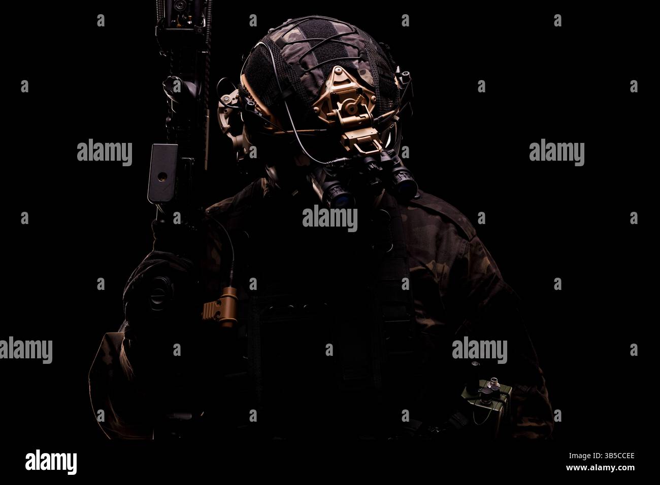 Ein Soldat in taktischer militärischer Ausrüstung, mit einem Gewehr, in einer schwach beleuchteten Umgebung. Zeigt Professionalität und Hightech-Ausrüstung für Sicherheit, Stockfoto