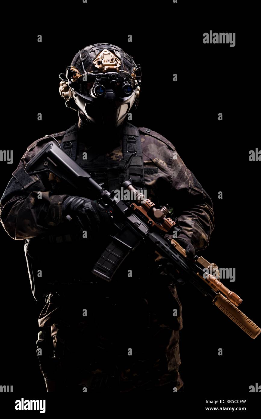 Ein Soldat, ausgestattet mit taktischer Ausrüstung einschließlich Gewehr und Nachtsichtbrille, fotografiert vor dunklem Hintergrund, symbolisiert Bereitschaft, stehlen Stockfoto