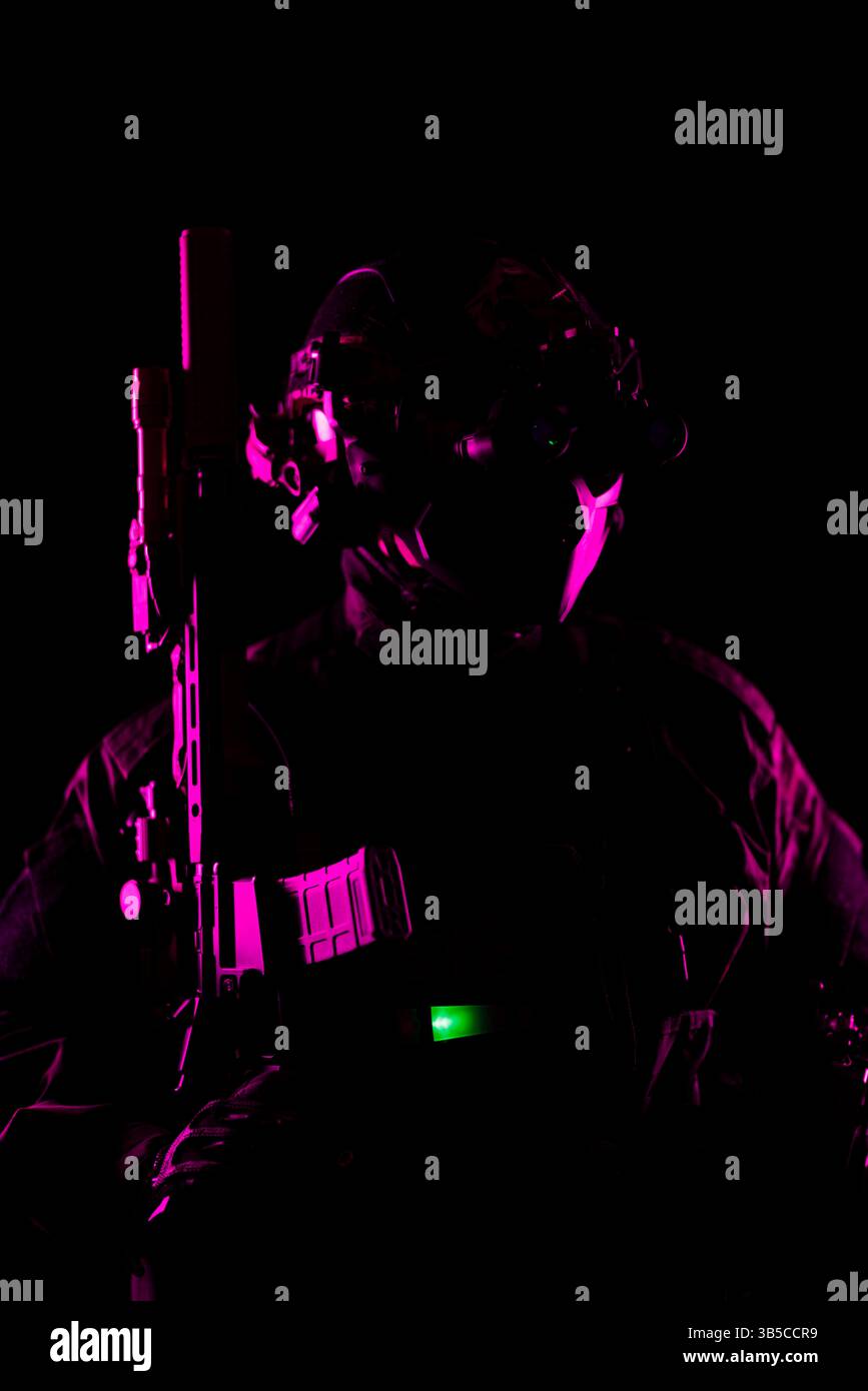 Eine künstlerische Fotografie bei schwachem Licht eines Soldaten in taktischer High-Tech-Ausrüstung und -Waffen, betont durch rosa und grüne Beleuchtung, die Schlüsseldetails beleuchtet, Stockfoto