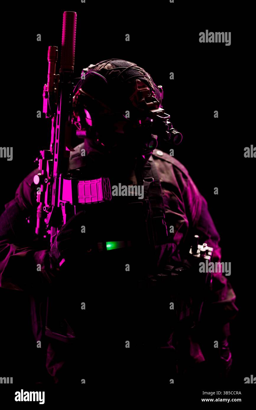 Gepanzerter Soldat mit fortschrittlicher taktischer Ausrüstung, hervorgehoben durch dramatische rosa und grüne Beleuchtung vor dunklem Hintergrund, die an Themen der tec erinnern Stockfoto