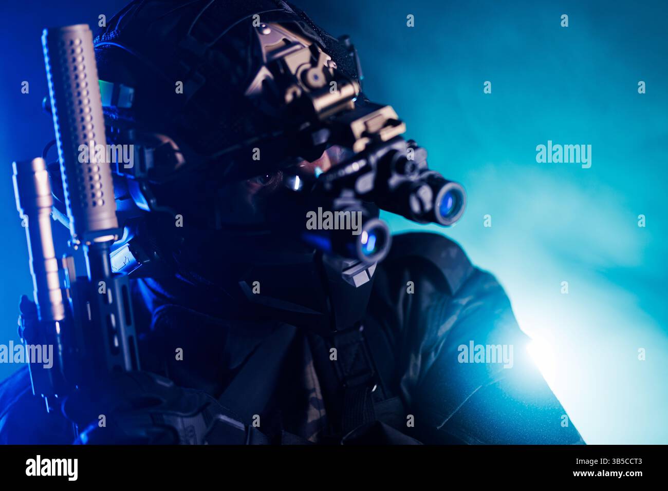 Nahaufnahme eines Spezialeinsatzfahrers, der mit Präzisionsgerät in einer dramatischen, blau beleuchteten Szene zielt. Mit fortschrittlicher Ausrüstung und Nachtsichtbrille, Stockfoto