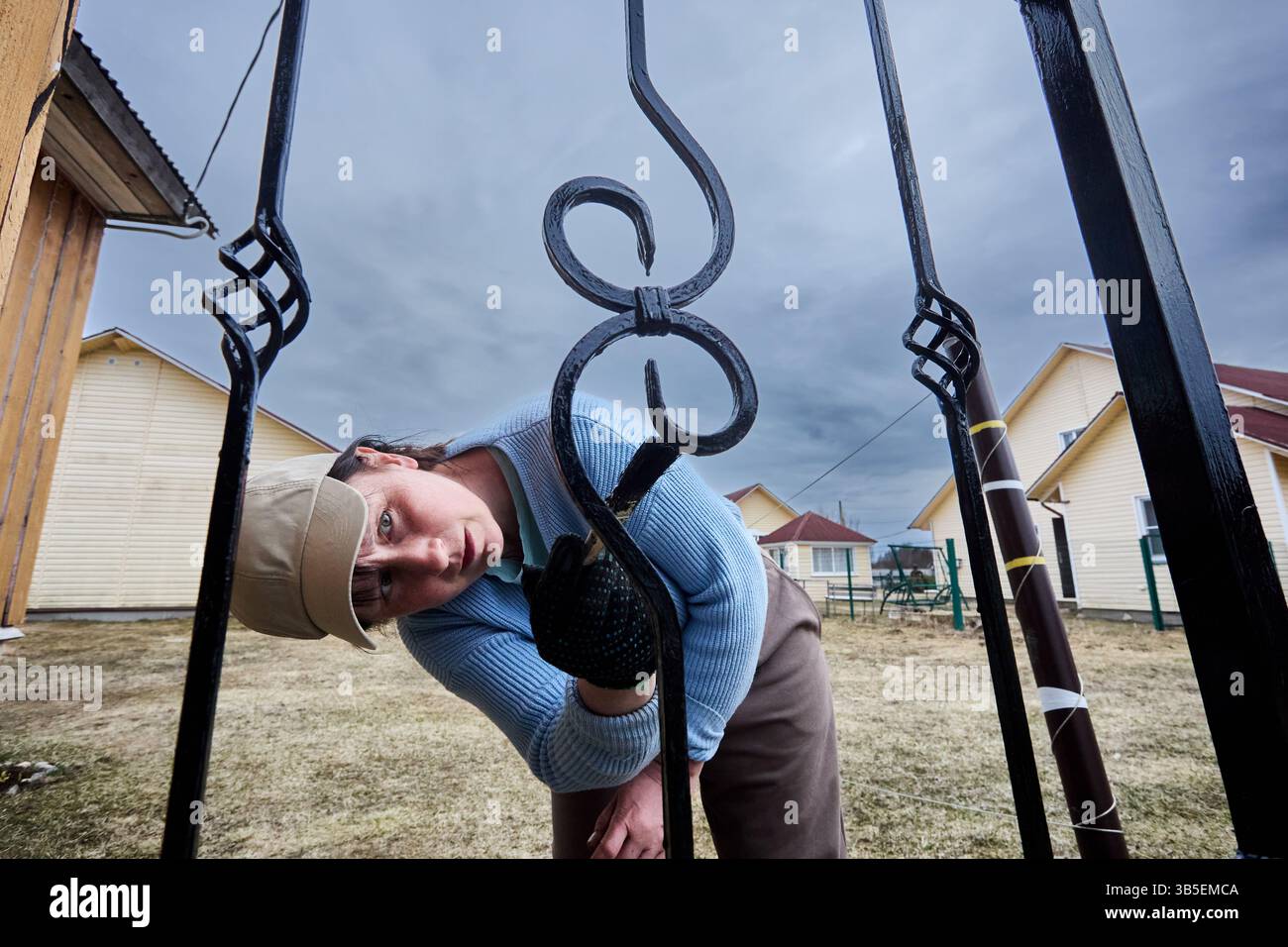 Schutzbeschichtung auf dekorative Elemente des Metallzauns der Eingangshalle, reife Kaukasierin mit kleinem Pinsel. Stockfoto