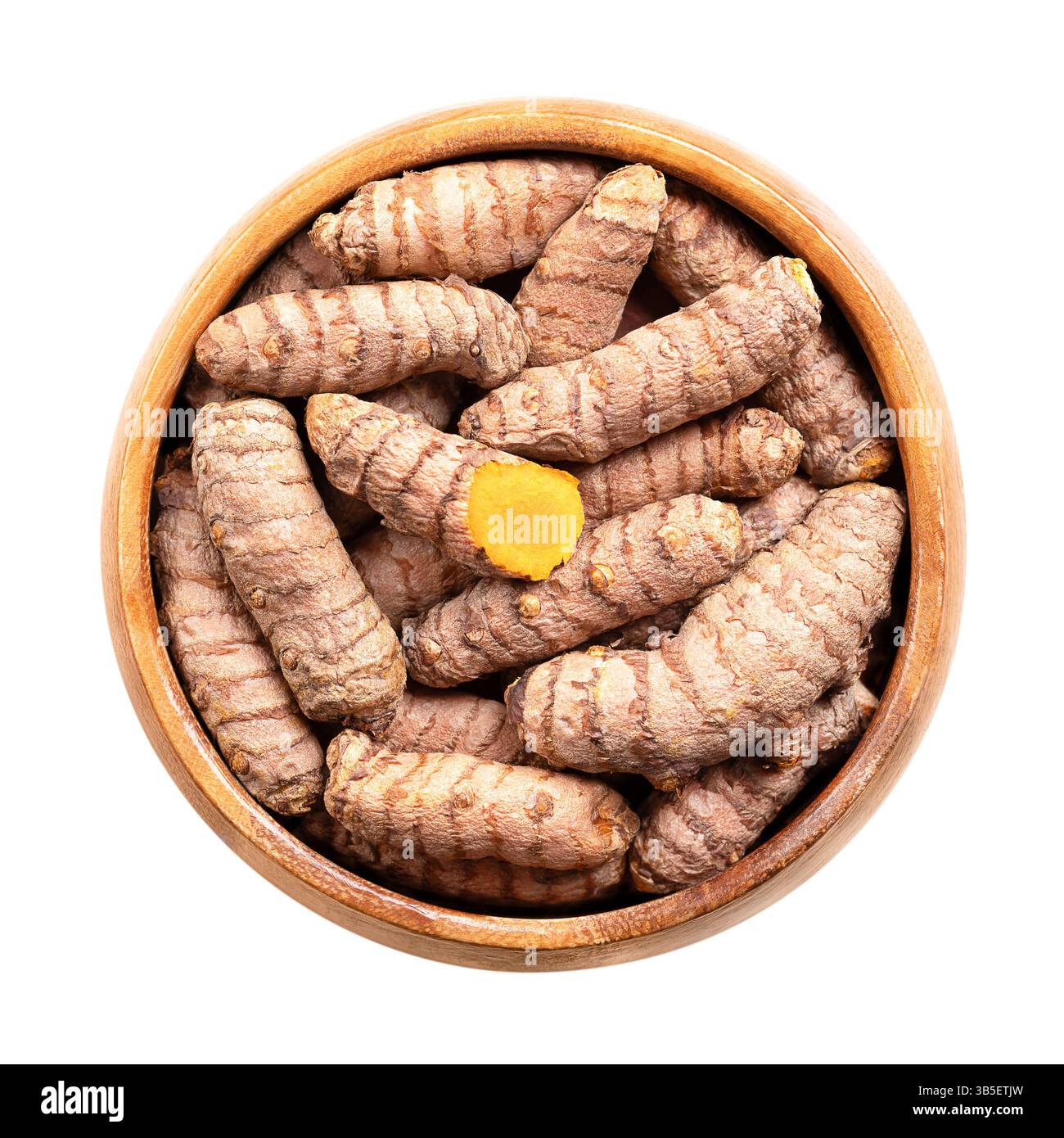 Frische Kurkuma-Rhizome in Holzschale. Unterirdische Stämme der Kurkuma-Pflanze Curcuma longa. Ein Stiel ist aufgeschnitten und zeigt das leuchtend orangefarbene Fleisch. Stockfoto
