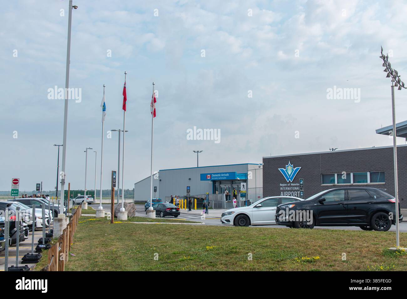 Reisende kommen am Inlandsterminal des internationalen Flughafens Region of Waterloo an, mit Fahrzeugen und Fahnen, die unter bewölktem Himmel sichtbar sind. Stockfoto
