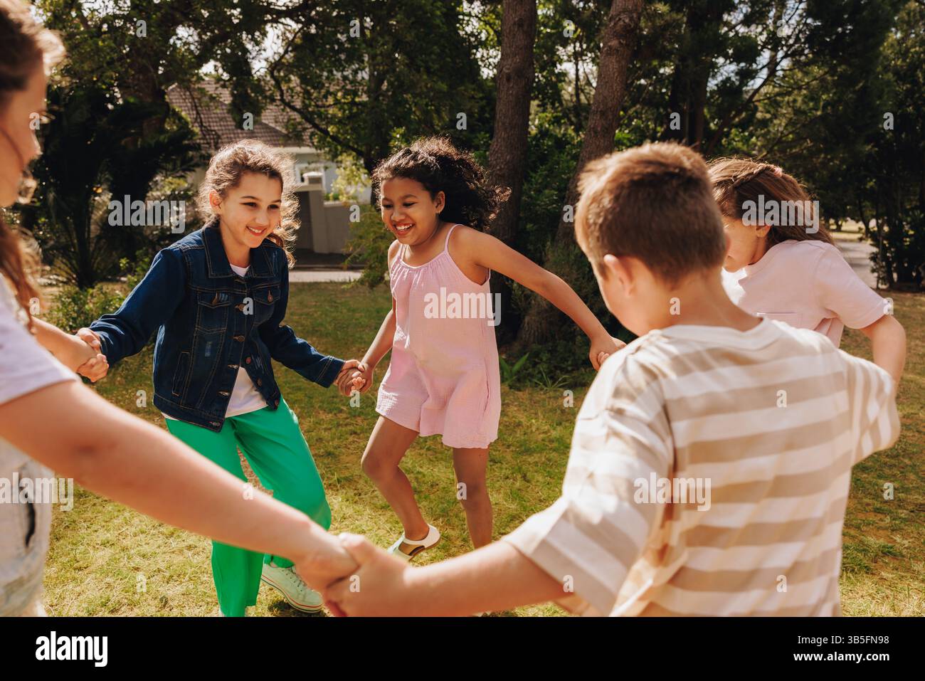 Eine Gruppe fröhlicher Kinder, die Hände halten, während sie gemeinsam in einem sonnigen Park spielen. Die Szene zeigt Freundschaft, Freude und den sorglosen Geist des Kindes Stockfoto