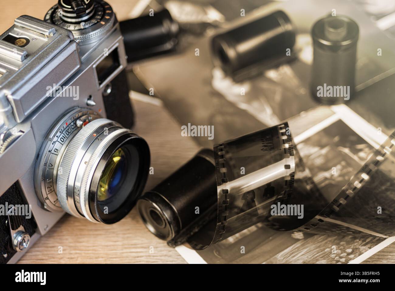 Eine Vintage-Kamera liegt auf einer Holzoberfläche, umgeben von Schwarz-weiß-Fotografien und Filmrollen, die Nostalgie für klassische Fotografien wecken. Stockfoto