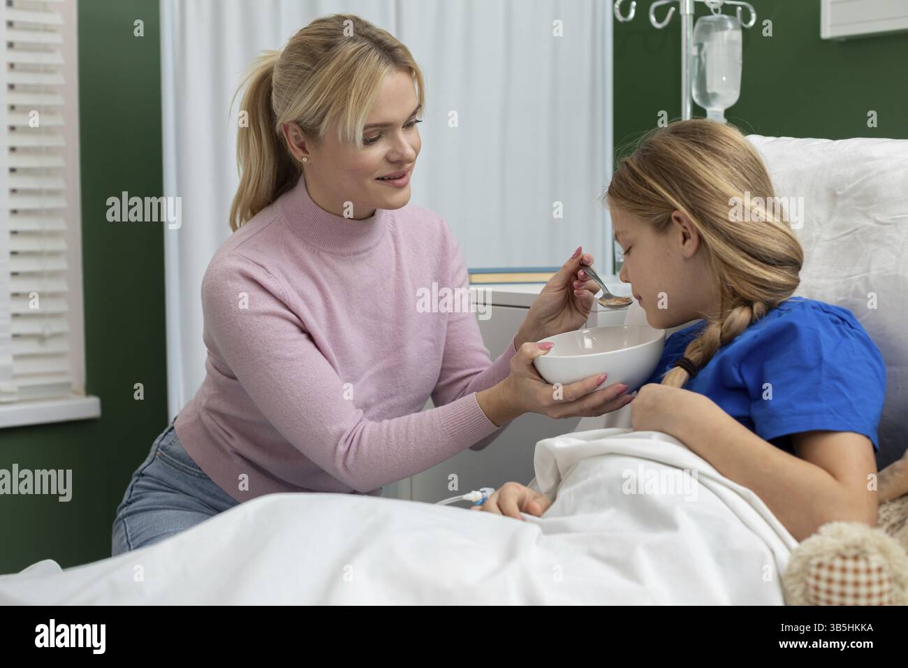 Eine engagierte und liebevolle Mutter sorgt für aufmerksame Pflege, indem sie ihre kranke Tochter ernährt, während sie in einem Krankenhauszimmer ist Stockfoto