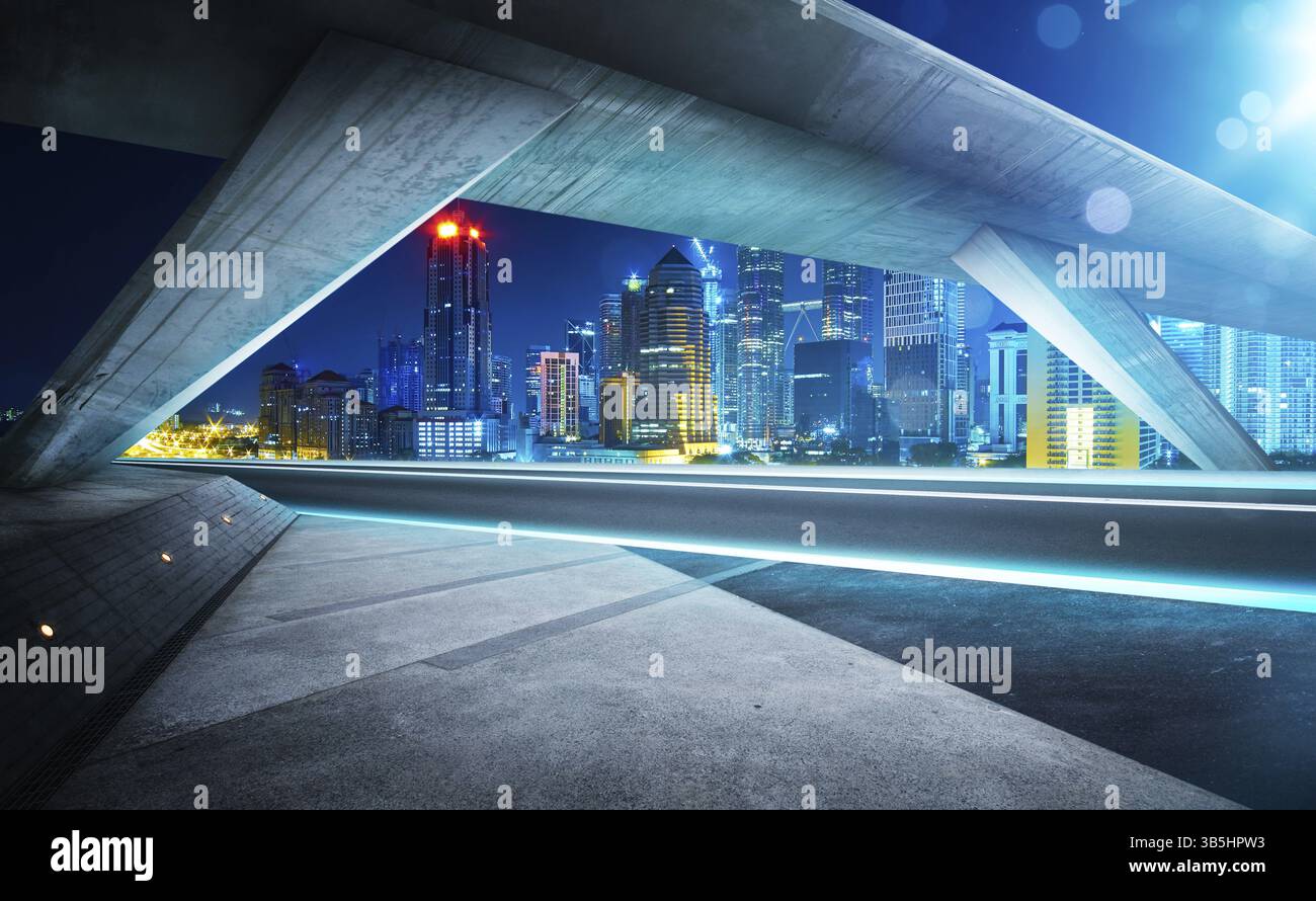 Leere Asphaltstrasse unter der Bruecke waehrend der Nacht mit schönstadt Skyline Hintergrund Stockfoto