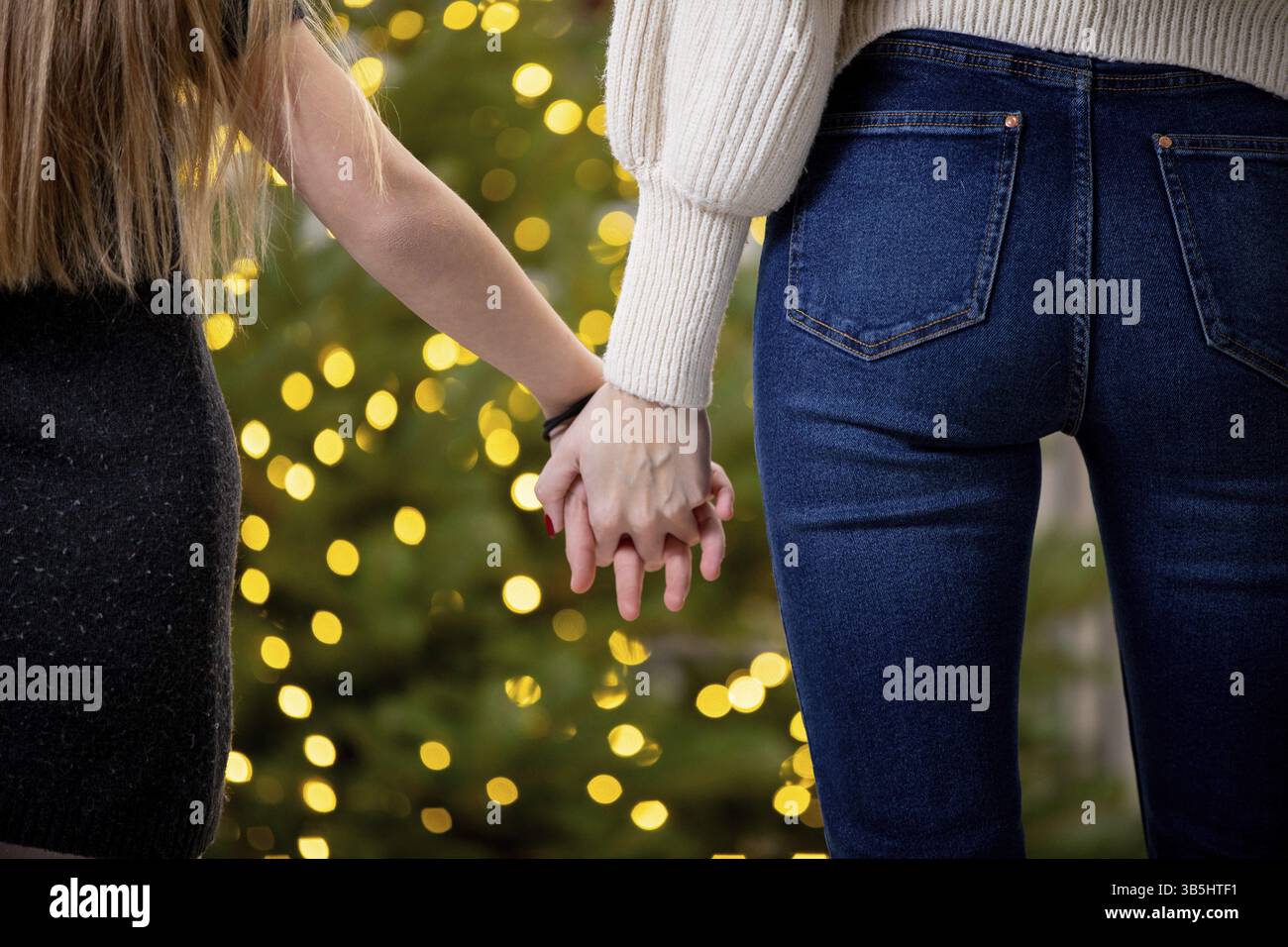 Ein romantischer Moment zwischen zwei Einzelpersonen, die Hände halten, umgeben von festlichen Lichtern, schaffen eine magische Atmosphäre Stockfoto