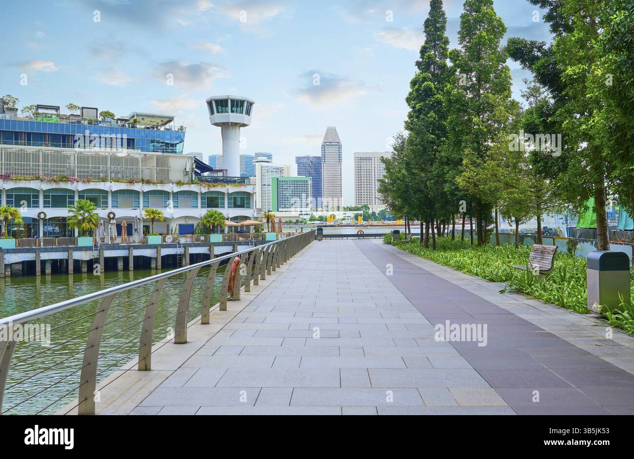 Modernes Stadtbild von singapur mit einer gepflasterten Promenade, die von Bäumen gesäumt ist, bietet malerische Ausblicke auf die Skyline der Stadt und das Wasser Stockfoto