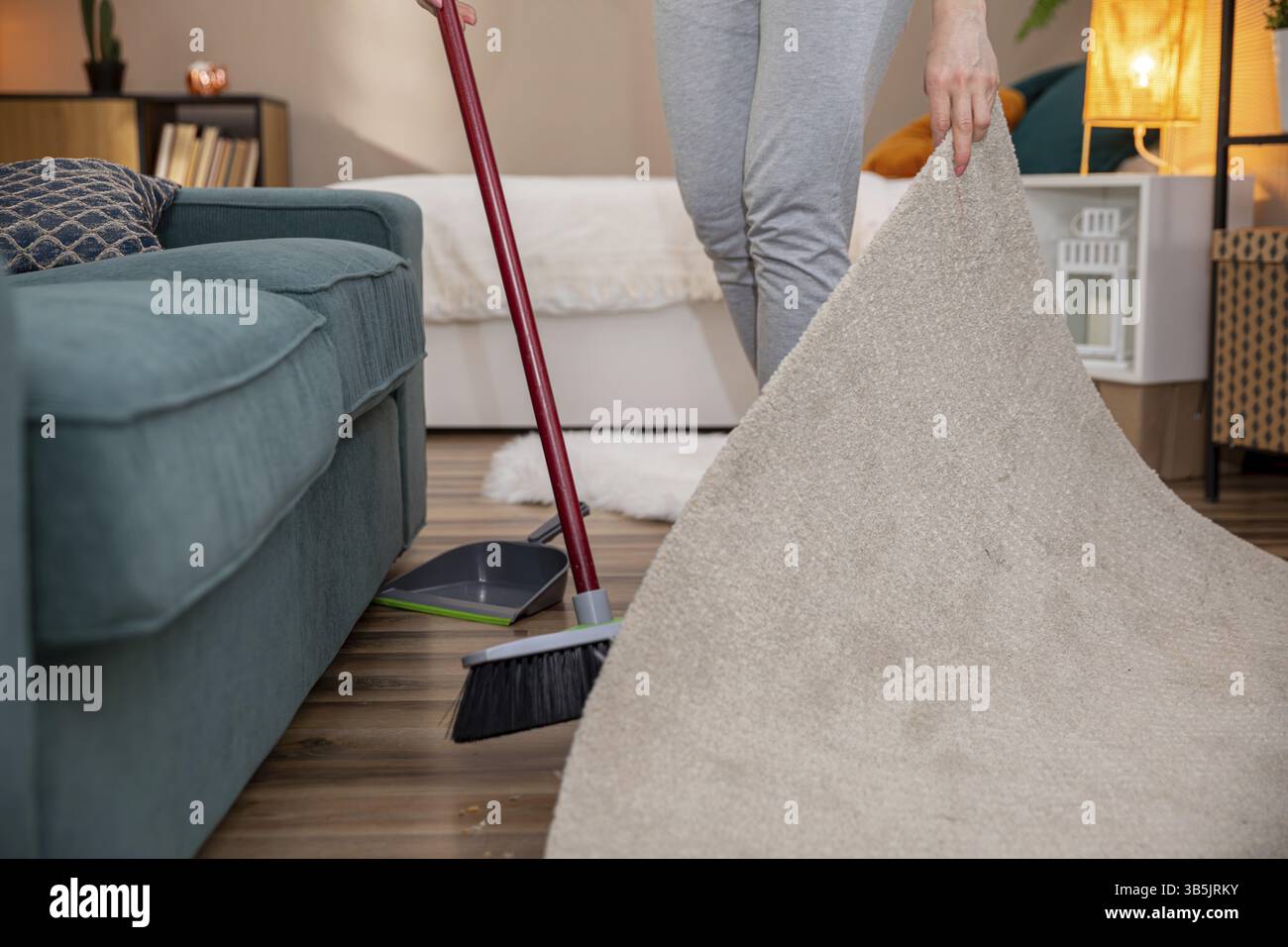 Eine Person reinigt aktiv ein Wohnzimmer, indem sie einen Teppich hochhebt und sicherstellt, dass der gesamte Raum aufgeräumt wird Stockfoto