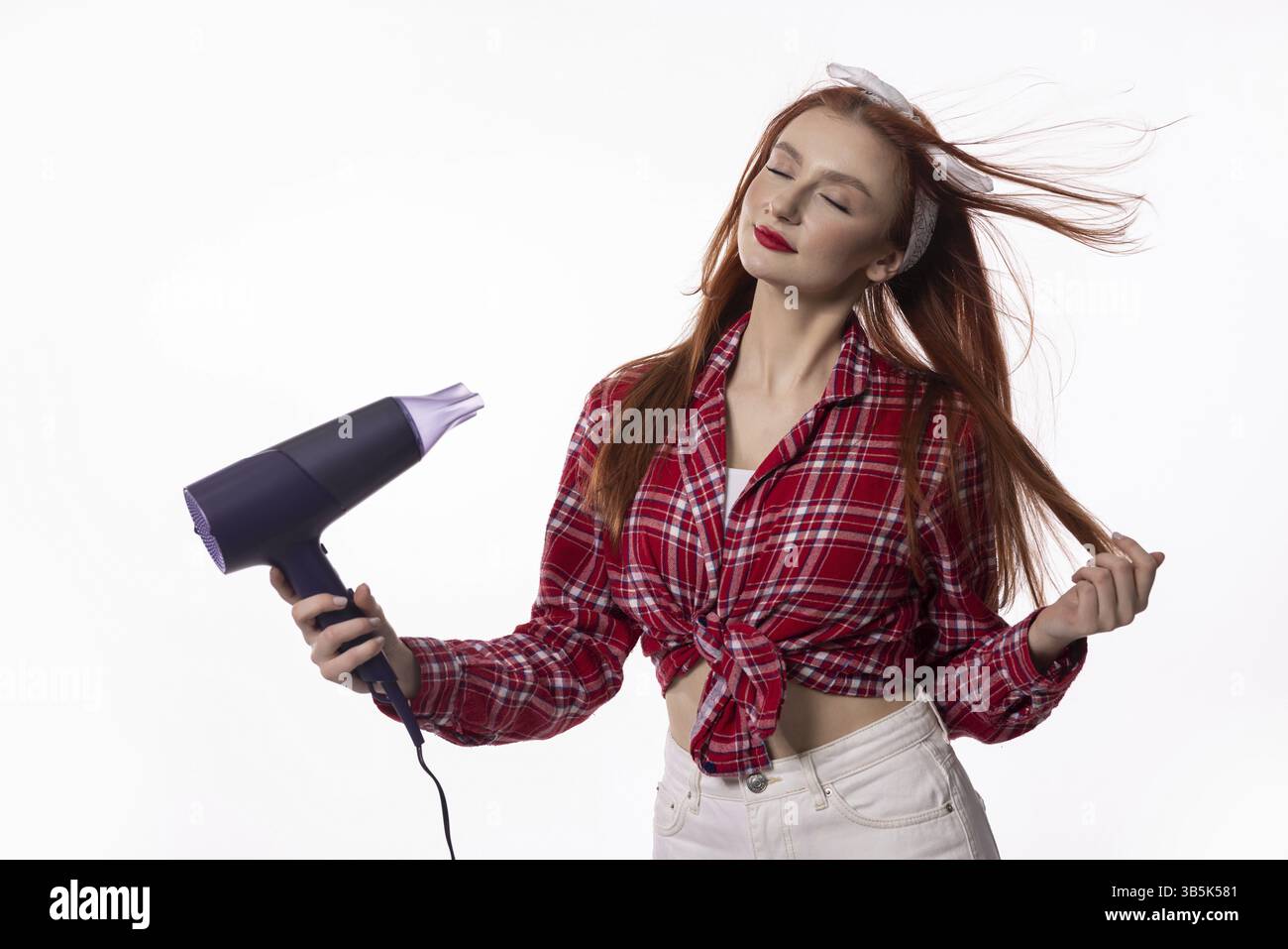 Eine stilvolle und selbstbewusste Frau nutzt geschickt einen Haartrockner und zeigt ihren Charme in einem modernen Studio Stockfoto