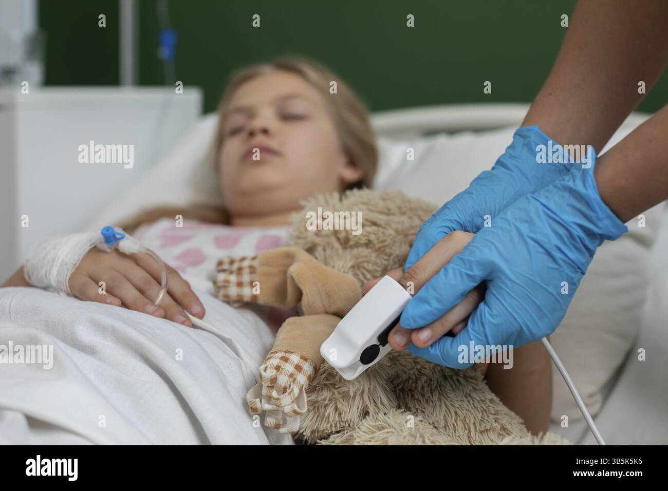 Ein Kind in einem Krankenhausbett, das betreut wird, einen beruhigenden Teddybären hält, umgeben von medizinischen Überwachungsgeräten Stockfoto