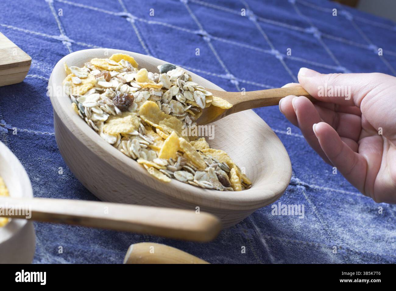 Weibliche Hand hob Getreide mit einem Holzlöffel aus Holzschale auf das Homeboard Stockfoto