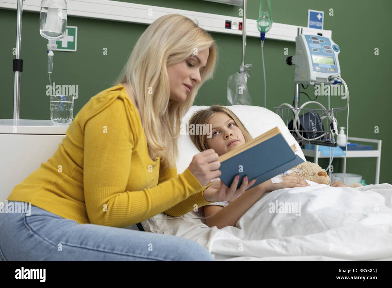 Eine beruhigende Szene, in der eine Mutter ihrem Kind in einem Krankenhausbett vorliest und dabei Liebe und Unterstützung betont Stockfoto