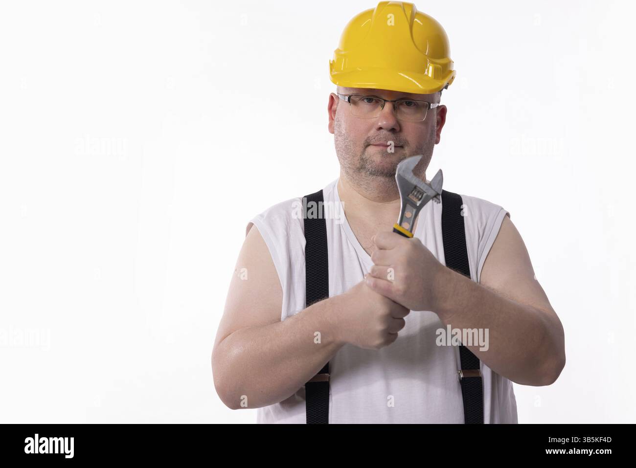 Ein Bauarbeiter in einem gelben Schutzhelm posiert mit einem schweren Schraubenschlüssel und ist bereit für die bevorstehenden Herausforderungen Stockfoto