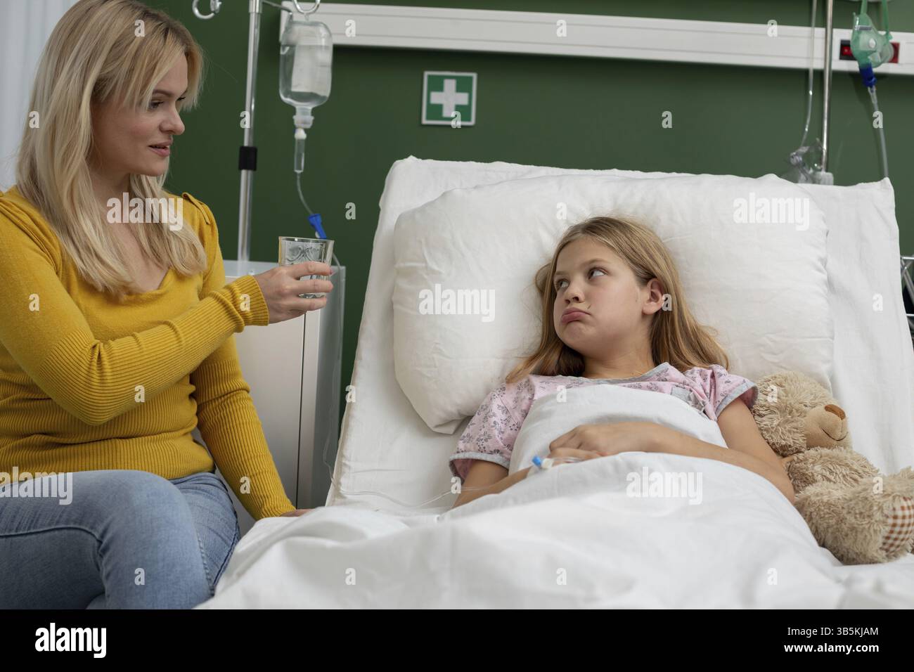 Eine fürsorgliche und aufmerksame Mutter schenkt ihrer Tochter sanft Wasser, die derzeit in einem Krankenhausbett liegt Stockfoto